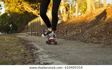 Young woman skate boarding along a cement path at sunset