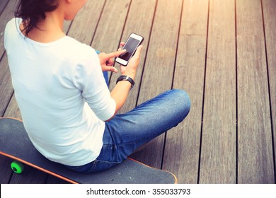 Young Woman Skateboarder Use Smartphone Sit On Skateboard