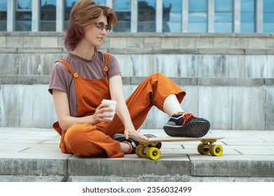 Young woman skater sitting on city steps with skateboard, holding white coffee container in her hand. Summer sports leisure. - Powered by Shutterstock