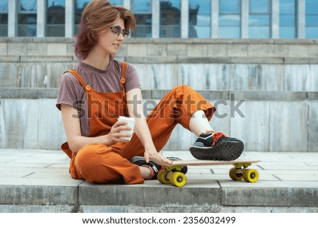 Young woman skater sitting on city steps with skateboard, holding white coffee container in her hand. Summer sports leisure.