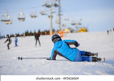 Young Woman Skier In Blue Ski Suit After The Fall On Mountain Slope Trying Get Up Against Ski-lift. Ski Resort. Winter Sports Concept.