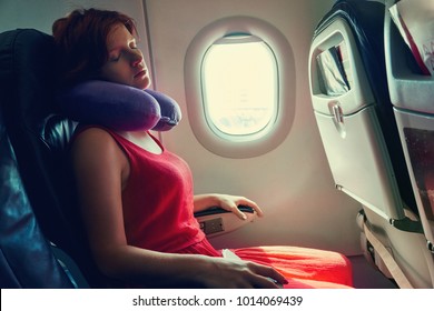 Young Woman Sleeping In An Airplane Seat. Traveler In An Plane With Pillow For Neck