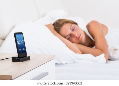 Young Woman Sleeping In Bed With Alarm On Mobile Phone Display