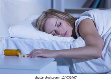 Young Woman Sleeping In Bed By Spilt Bottle Of Pills On Table At Home