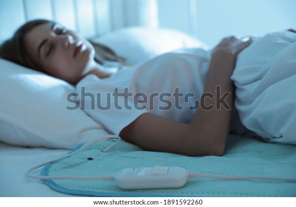 Young woman sleeping in bed with electric heating\
pad, focus on cable