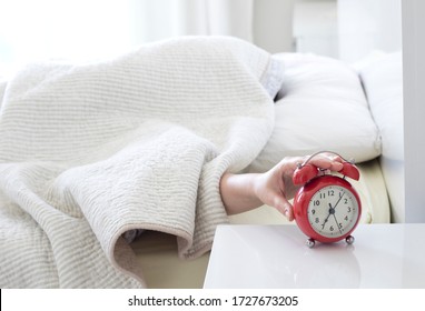 Young Woman Sleeping On Bed Pressing Snooze Button On Black Vintage Alarm Clock At Seven O'clock Morning In Bed Room At Home, Lifestyle, Good Morning, Healthy Sleep And Joyful Weekend Concept