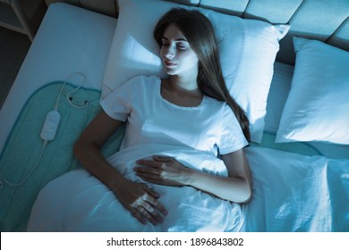 Young Woman Sleeping On Electric Heating Pad In Bed At Night, Top View