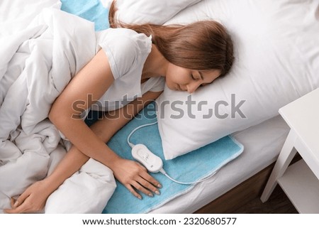 Young woman sleeping on electric heating pad in bedroom