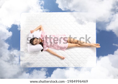 Young woman sleeping on mattress soft as clouds in blue sky