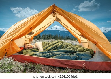 Young woman sleeping under a down blanket in a yellow tent in the morning mountains. - Powered by Shutterstock