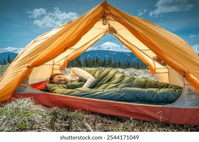 Young woman sleeping under a down blanket in a yellow tent in the morning mountains. - Powered by Shutterstock