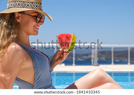 Young woman with slice of watermelon in straw hat sunbathing sitting on the edge of swimming pool