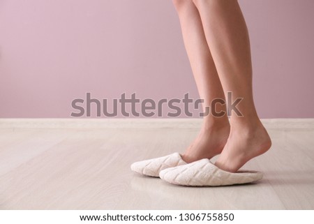 Young woman in slippers against color wall