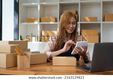 Young woman small business owner online shopping at home. confirm orders from customers with mobile phones preparing package product on background. SME entrepreneur or freelance life style concept.