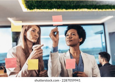 Young woman of a small company putting an adhesive note on glass in office during team meeting formulating business strategies. - Shutterstock ID 2287059941