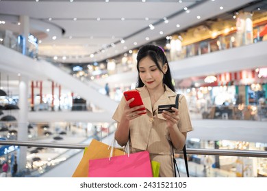 young woman in smart casual wear carrying many paper shopping bags shopping online on mobile phone using credit card at shopping center - Powered by Shutterstock