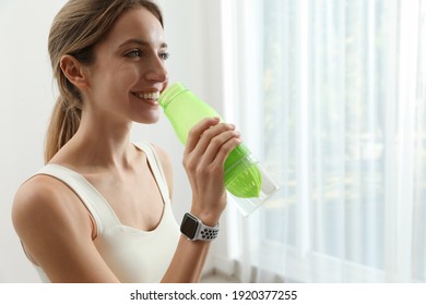 Young woman with smart watch drinking water indoors, space for text
