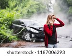 A young woman with smartphone by the damaged car after a car accident, making a phone call.