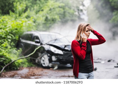 A young woman with smartphone by the damaged car after a car accident, making a phone call. - Shutterstock ID 1187006293