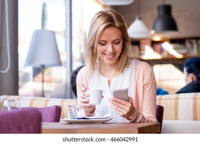 Young woman with smartphone in cafe drinking coffee