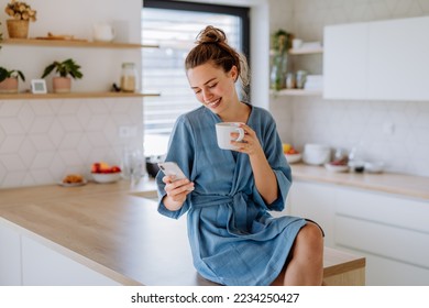 Young woman with smartphone enjoying cup of coffee at morning, in her kitchen. - Powered by Shutterstock