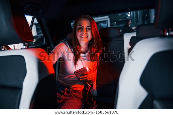 Young woman with smartphone is inside of\
brand new modern\
automobile.