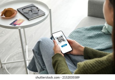 Young woman with smartphone scanning QR code at home