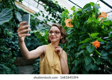 Young woman with smartphone standing in botanical garden, taking selfie. - Powered by Shutterstock