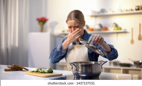 Young Woman Smelling Cooked Soup With Disgusted Face Expression, Spoiled Food