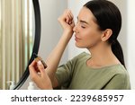 Young woman smelling essential oil on wrist indoors