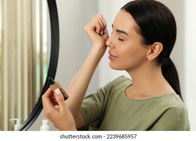 Young woman smelling essential oil on wrist indoors - Shutterstock ID 2239685957