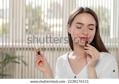 Young woman smelling essential oil indoors, space for text