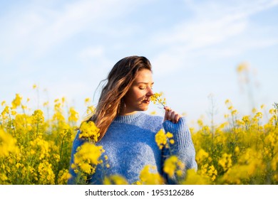 Young Woman Smelling Yellow Flowers In A Field