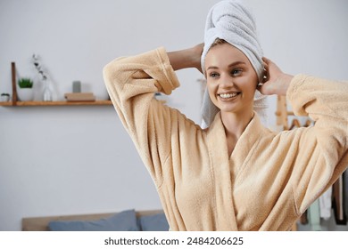 A young woman smiles brightly, wearing a soft, tan robe and a towel wrapped around her head. - Powered by Shutterstock