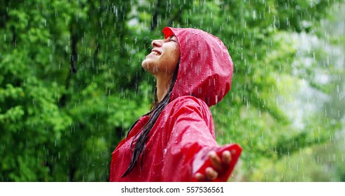 The young woman smiles and laughs under the rain. the rain falls, the drops fall on her face and she is happy with life and nature around. concept of nature and happy life, adventure, purity