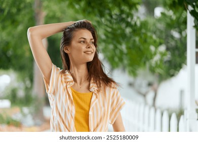 Young woman smiling in a bright striped shirt outdoors, surrounded by greenery and a white picket fence Fresh and vibrant atmosphere suitable for relatable lifestyle imagery - Powered by Shutterstock