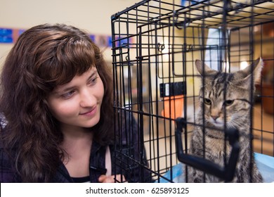 Young Woman Smiling By Cage With One Young Cat Waiting For Adoption