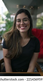 Young Woman Smiling At Camera Portrait. Girl In 20s Wearing Eyeglasses. Person Big Smile Seated At Coffee Shop In Vertical Video SS