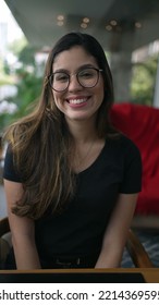 Young Woman Smiling At Camera Portrait. Girl In 20s Wearing Eyeglasses. Person Big Smile Seated At Coffee Shop In Vertical Video SS