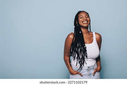 Young woman smiling at the camera while standing against a blue background. Young black woman feeling confident in her style. - Powered by Shutterstock