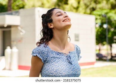 Young Woman Smiling Confident Wearing Summer Dress Standing On City Park, Outdoors Closes Her Eyes And Relaxes With A Big Smile. The Concept Of Meditation Outside.