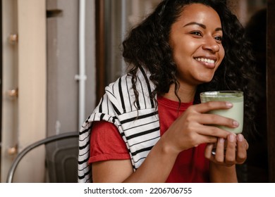 Young Woman Smiling And Drinking Matcha Latte While Sitting At Cafe Outdoors