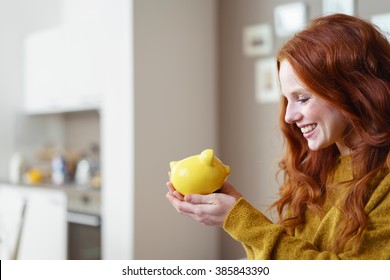 Junge Frau lächelt fröhlich an ihrem gelben Keramikschweinchen, das sie in den Händen hält, während sie erwartet, ihr Nestei auszugeben