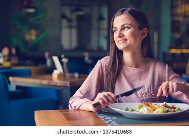 Young woman smiling and looking away while eating lunch at the restaurant. Thoughtful, content, happy, free, single. 