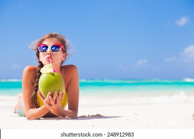 young woman smiling lying in straw hat in sunglasses with coconut on beach