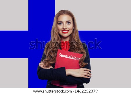 Young woman smiling and posing against the Finnish flag background. Finnish language school and travel concept. Book with inscription Finnish on finnish language