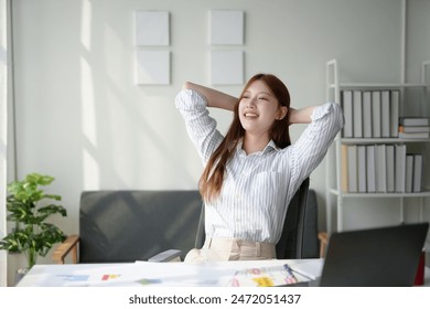 Young woman smiling and relaxing in a bright office, enjoying a break at work with hands behind her head. - Powered by Shutterstock