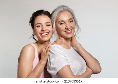 Young woman and smiling senior lady hugging portrait. Modest shy millennial daughter covering face with palm cuddling confident experienced aged mother from back. Trust protection, love support