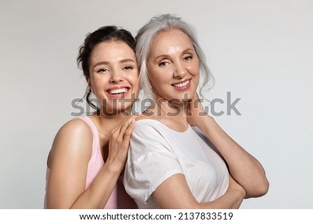 Young woman and smiling senior lady hugging portrait. Modest shy millennial daughter covering face with palm cuddling confident experienced aged mother from back. Trust protection, love support