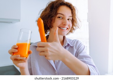 young woman smiling showing thumbs up sign to super carrot fresh in home kitchen. teenage who drinks vitamin drink in morning from freshly squeezed carrot juice enriched with carotene and vitamin A - Shutterstock ID 2168903129